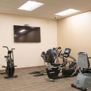 A small gym room with various exercise equipment, including stationary bikes and treadmills, facing a wall-mounted television.
