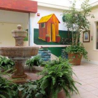 A serene indoor courtyard featuring a fountain surrounded by lush greenery and a colorful mural on the wall.