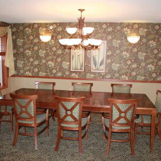 A dining room featuring a long wooden table with matching chairs, decorative wallpaper, and an elegant chandelier overhead.