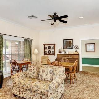 A cozy living room with a floral sofa and dining area, featuring a ceiling fan and decorative elements.