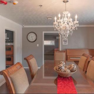 A dining room with a chandelier, table, and chairs, featuring elegant decor and a wall clock.