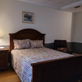 A cozy bedroom featuring a wooden bed with patterned bedding, a nightstand with a lamp, and wall decor.