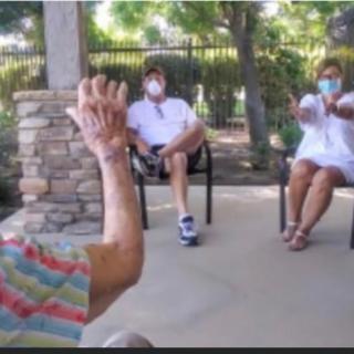 A group of people sitting outdoors, wearing masks and maintaining social distance.