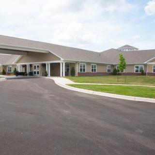 A single-story building with a covered entrance and a wide driveway leading to it, surrounded by well-maintained lawns.