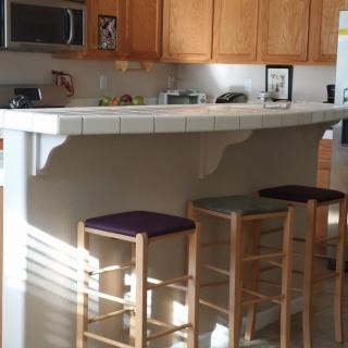 A cozy kitchen with a tiled counter and bar stools, illuminated by sunlight.