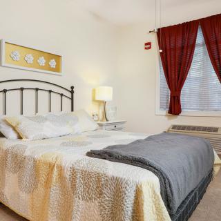 A cozy bedroom with a neatly made bed, bedside lamp, and red curtains.