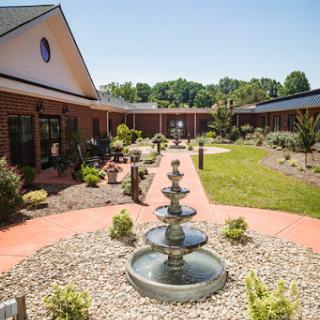 A serene courtyard featuring a decorative fountain surrounded by well-maintained gardens on a sunny day.