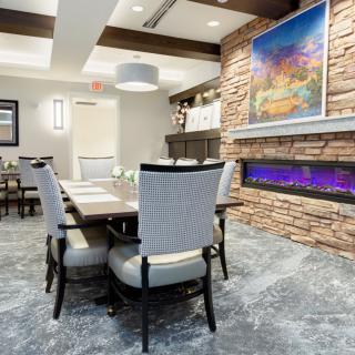 A modern dining room featuring a sleek table and chairs set, with a vibrant piece of artwork above a stone fireplace.