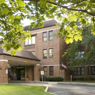 A brick building surrounded by trees with a road leading to the entrance.
