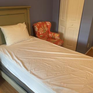 A cozy bedroom featuring a single bed with white bedding and a floral armchair.