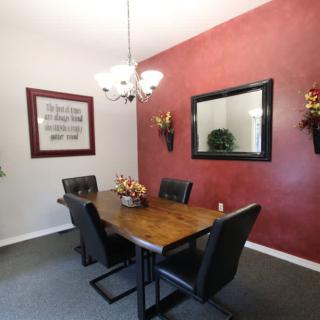 A modern dining room with a wooden table and black chairs, featuring a red accent wall with decorative elements and a mirror.
