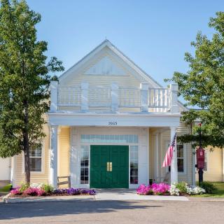 Front view of a building with a green door, flanked by trees and colorful flowers.