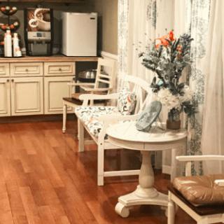 A cozy living room with vintage-style furniture, wooden flooring, and decorative flowers.