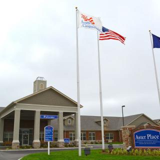 A building entrance with multiple flags and a sign on a cloudy day.