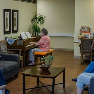 An elderly woman plays the piano in a cozy living room setting.
