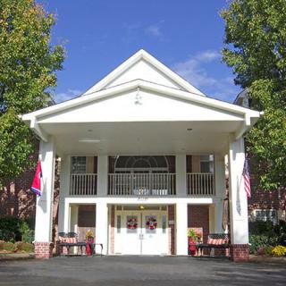 A building entrance with a white porch, flanked by trees and flags.