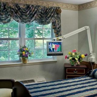 A well-decorated hospital room with a bed, television, and floral arrangements near the window.