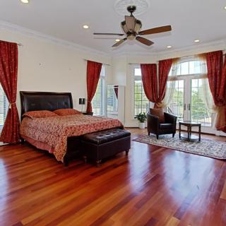 Spacious bedroom with wooden floors, large windows, and elegant red curtains.