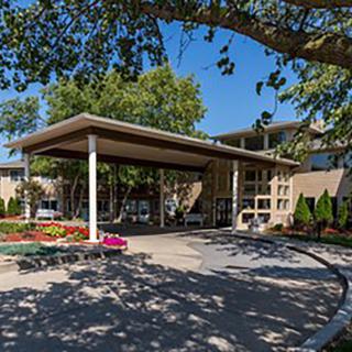 A building entrance with a covered driveway surrounded by trees and colorful flowers.