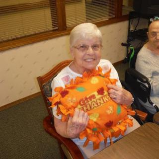 An elderly woman smiles while holding a colorful pillow, enjoying a moment indoors.