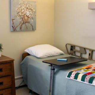 A cozy hospital room with a single bed covered in a quilt, featuring a side table and wall art.