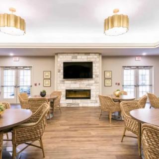 A cozy living room featuring wicker chairs and tables, a fireplace, and a wall-mounted television under elegant lighting.