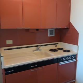A compact modern kitchen featuring a sink, stove, and cabinetry in warm tones.