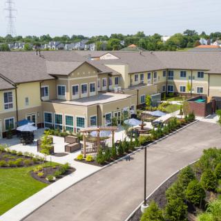 Aerial view of a residential building surrounded by landscaped greenery and a driveway.