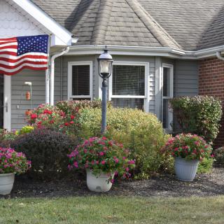 A suburban house with a well-maintained garden, featuring an American flag and various potted plants and shrubs.