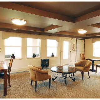 A cozy living room featuring armchairs, a round glass table, and ample natural light through multiple windows.
