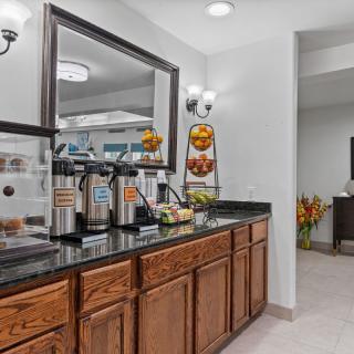 A cozy hotel breakfast area featuring a coffee station with beverage dispensers and assorted fruits on a granite countertop.
