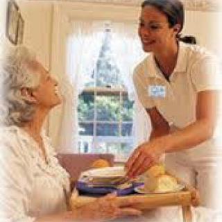 A caregiver providing meal service to an elderly woman in a home setting.