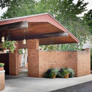 A modern brick building entrance with a distinctive overhanging roof and surrounding greenery.
