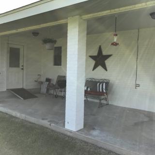 A covered porch with benches, a star decoration on the wall, and a concrete floor.