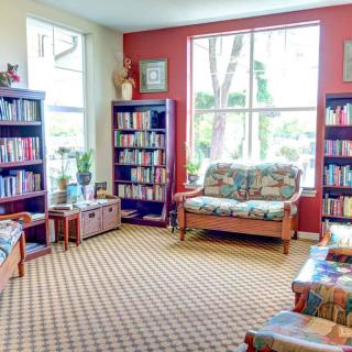 A cozy library reading area with bookshelves, sofas, and large windows.