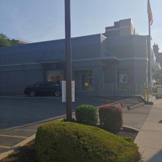 A commercial building with a parking lot and flags, surrounded by neatly trimmed bushes.