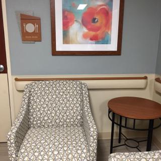 A waiting room with patterned chairs, a small table, and colorful artwork on the wall.