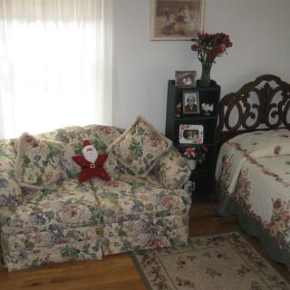 A cozy living space featuring a floral-patterned sofa with decorative pillows and a bed in a well-decorated room.