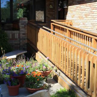 A sunny garden scene with potted flowers and a wooden railing by a house exterior.