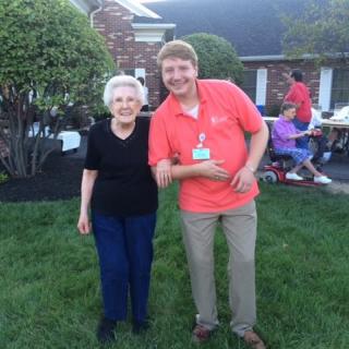 Two people smiling and posing together outdoors near a house.