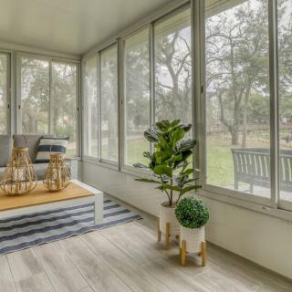 A cozy sunroom with large windows, featuring potted plants and a stylish wooden floor.