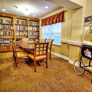 A cozy library room with a wooden table and chairs surrounded by bookshelves, featuring a popcorn cart by the window.