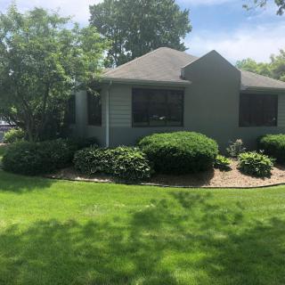 A well-maintained house with a lush green lawn and neatly trimmed bushes on a sunny day.