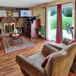 A cozy living room with a fireplace, armchair, and television, featuring hardwood floors and a view through the sliding glass door.