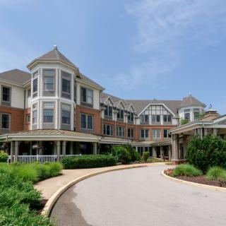 A large residential building with a circular driveway and landscaped gardens under a clear blue sky.