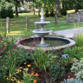 A beautiful garden scene featuring a two-tiered fountain surrounded by vibrant flowers and lush greenery.
