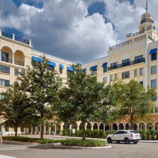 A grand hotel building with arched windows and a decorative tower, set against a cloudy sky, surrounded by trees and parked cars.