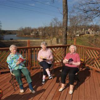 Three elderly women enjoying a sunny day while reading on a deck.