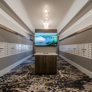 A modern hallway with mailboxes lining the walls and a central screen display.