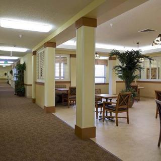 A spacious interior hallway with tables, chairs, and potted plants.